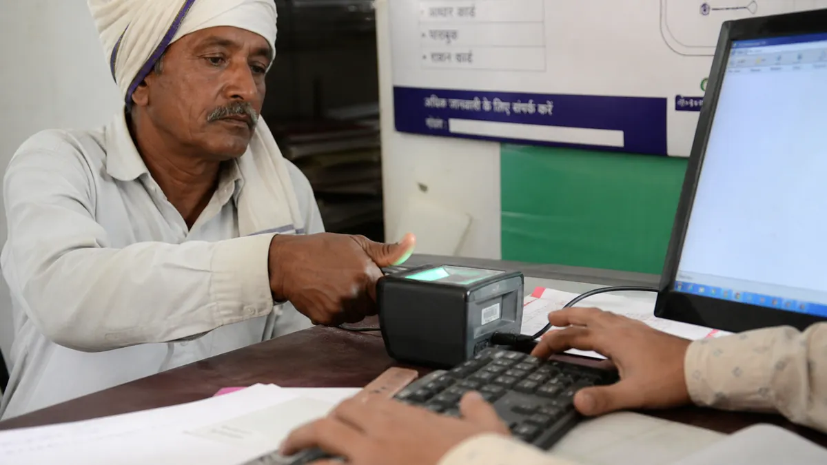 Biometric सत्यापन के लिए fingerprint scanner पर अंगूठा लगाता किसान